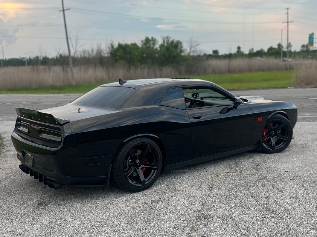 Black Dodge Challenger SRT 392 parked in a lot, featuring black five-spoke wheels, a rear spoiler, lowered stance, and performance suspension.