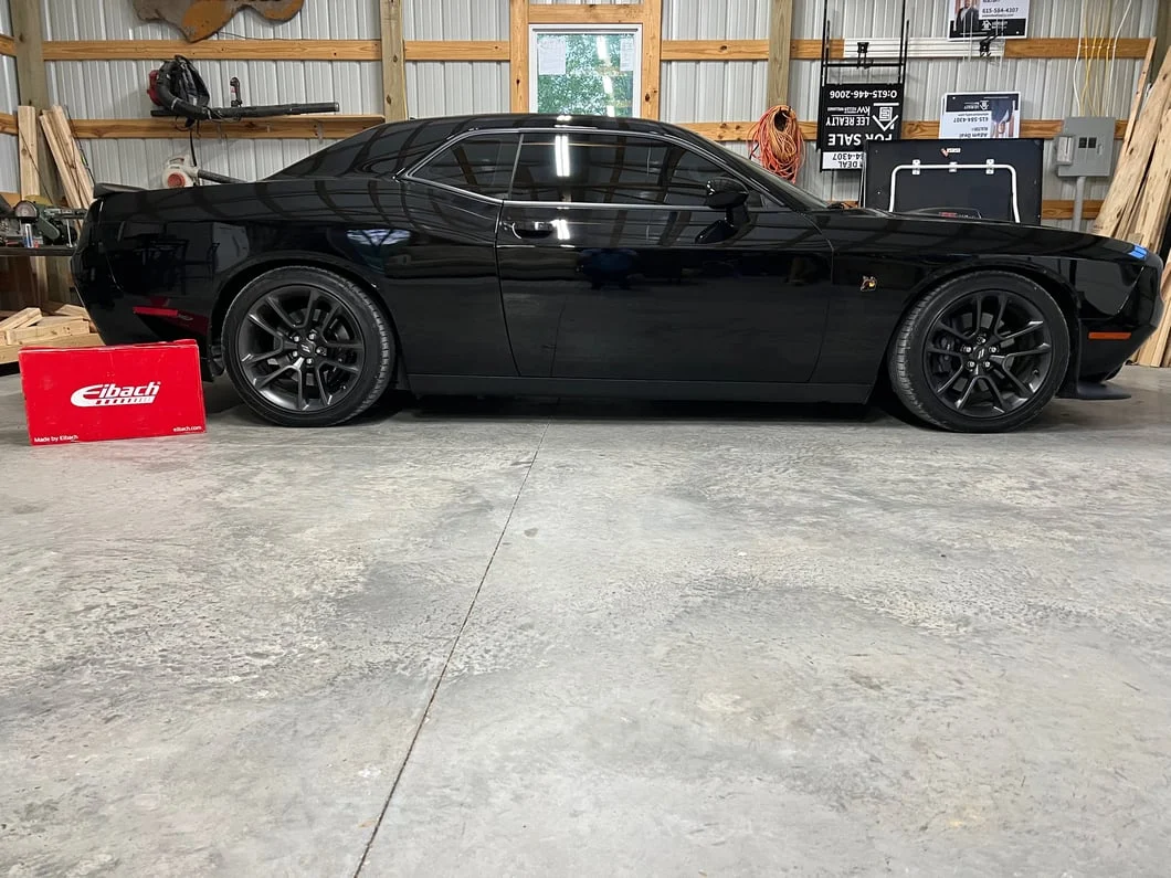 Black Dodge Challenger SRT 392 parked in a lot, featuring black five-spoke wheels, a rear spoiler, lowered stance, and performance suspension.