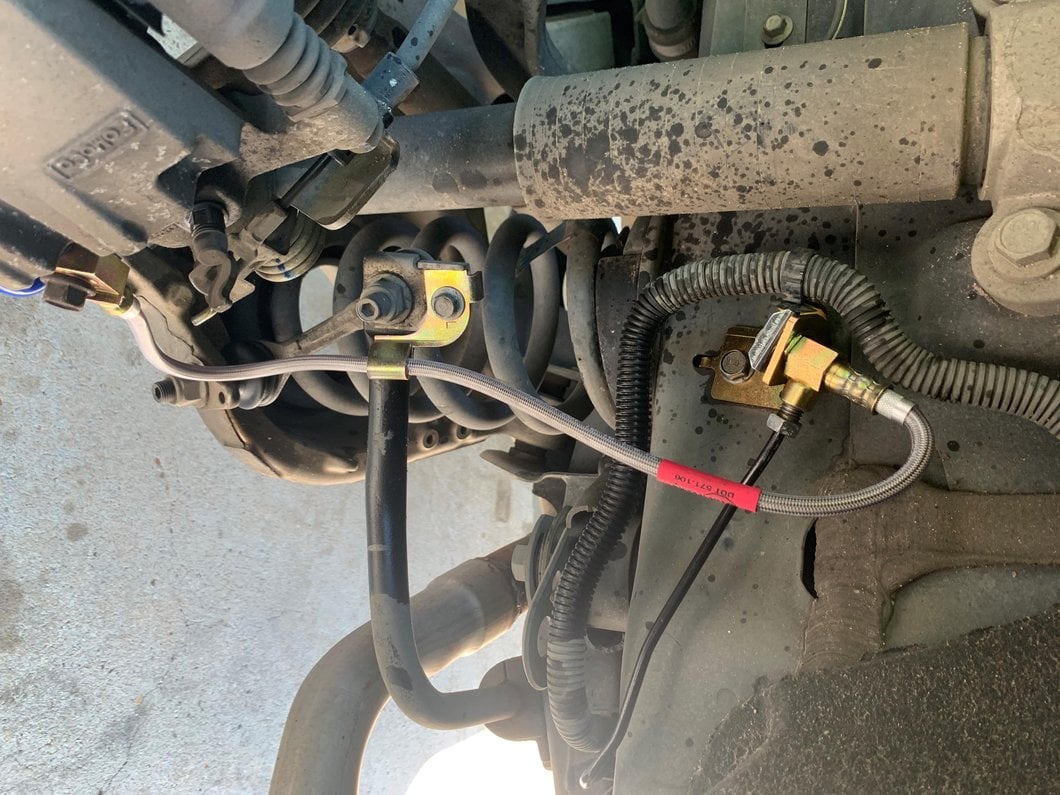 Stainless steel braided rear brake line installed on a vehicle's rear suspension, connecting the hard brake line to the axle to improve brake pedal feel, durability, and braking performance.