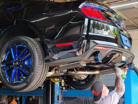 Technician installing a cat-back exhaust system on a late-model Ford Mustang raised on a vehicle lift, showing polished exhaust tips, rear suspension, and underbody exhaust components.