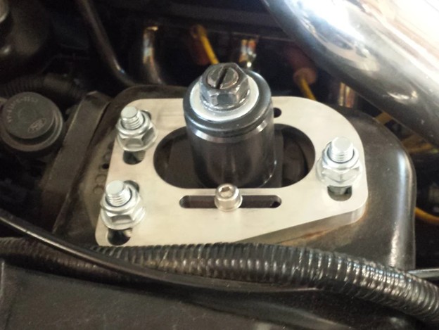 Adjustable caster/camber plate installed on a vehicle's front strut tower, allowing suspension alignment changes to fine-tune camber and caster angles.