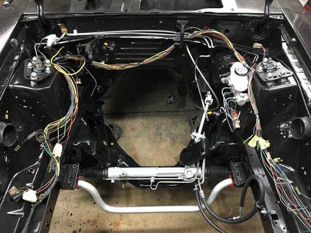 Engine bay with the engine removed, showing adjustable caster/camber plates installed on the front strut towers as part of a suspension and steering rebuild.