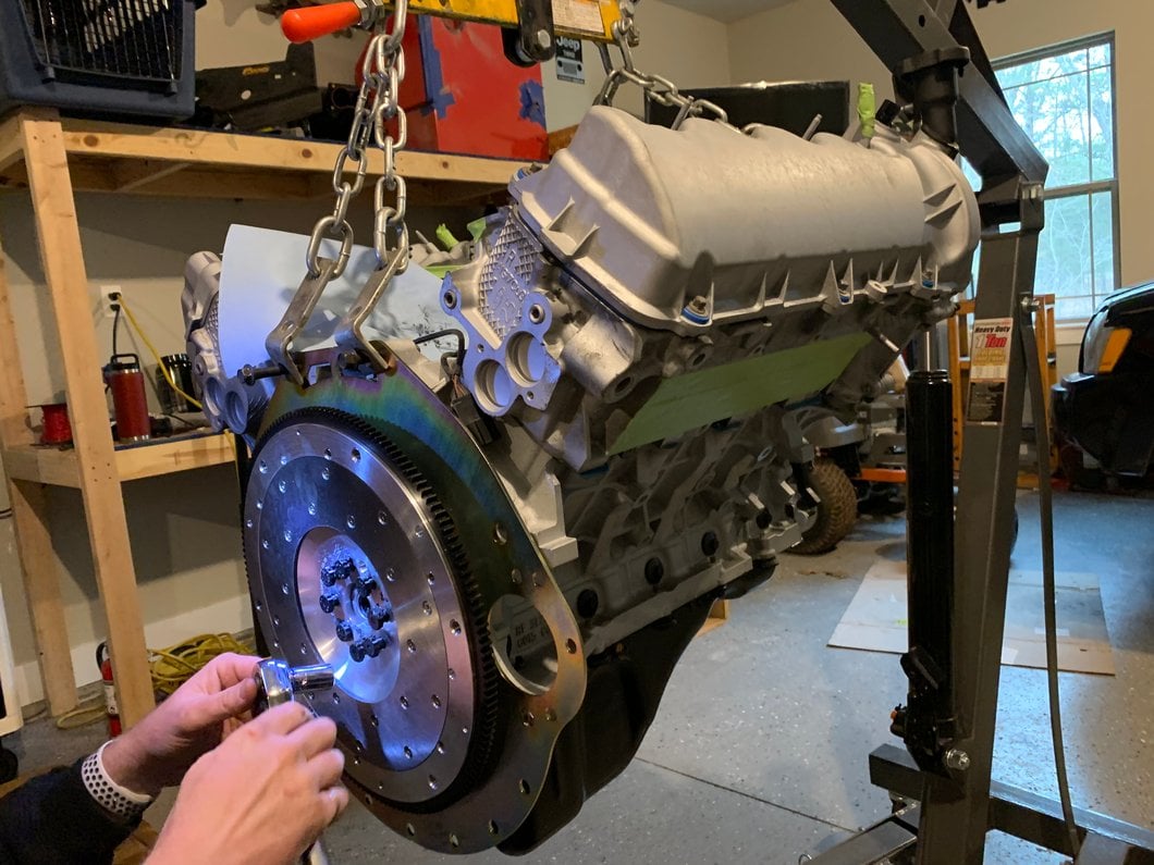 Performance flywheel being installed on a Ford Mustang V8 engine suspended from an engine hoist during an engine or clutch installation.