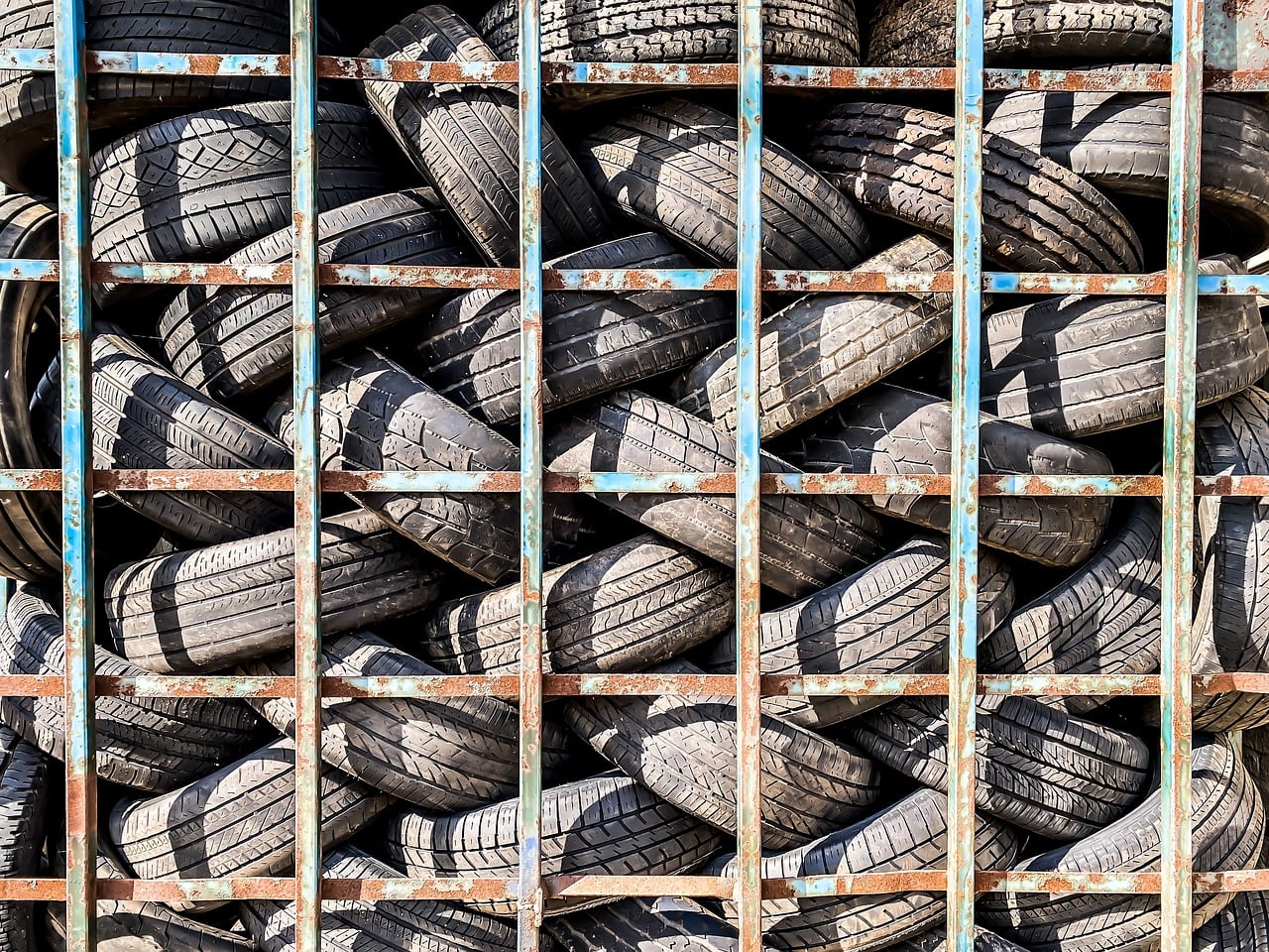 Stack of used vehicle tires stored in a metal recycling container at an automotive recycling facility.
