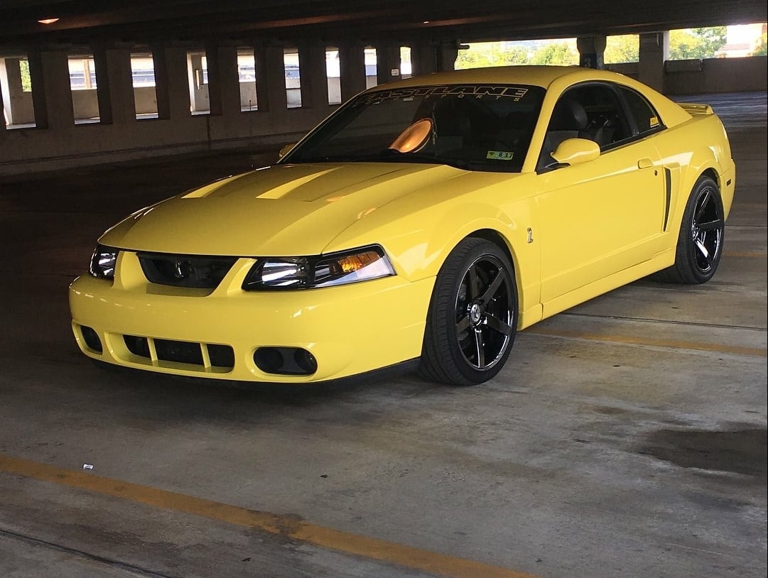 Yellow 2003&ndash;2004 Ford Mustang SVT Cobra Terminator with black aftermarket wheels parked in a parking garage.