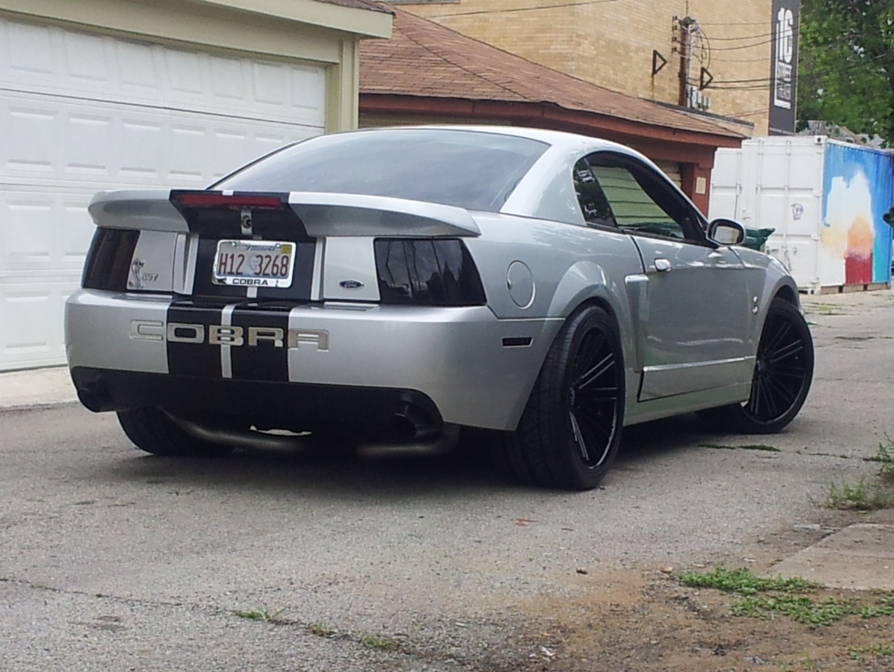 Silver 2003&ndash;2004 Ford Mustang SVT Cobra Terminator with black wheels, smoked taillights, and Cobra rear bumper graphics parked in an alley.