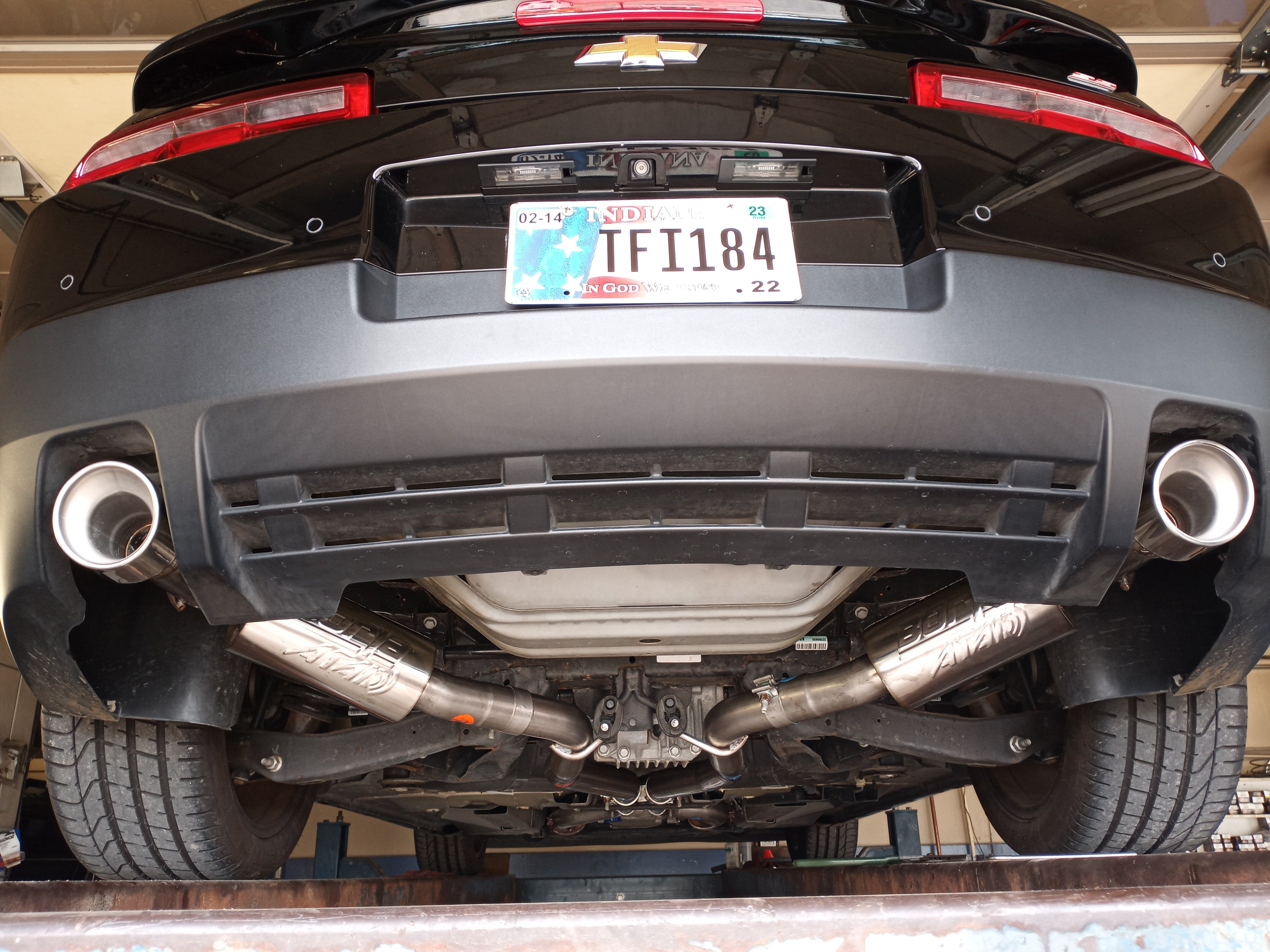 Rear underside view of a Chevrolet Camaro with a dual-exit cat-back exhaust system, featuring polished performance mufflers, stainless steel piping, and polished exhaust tips.