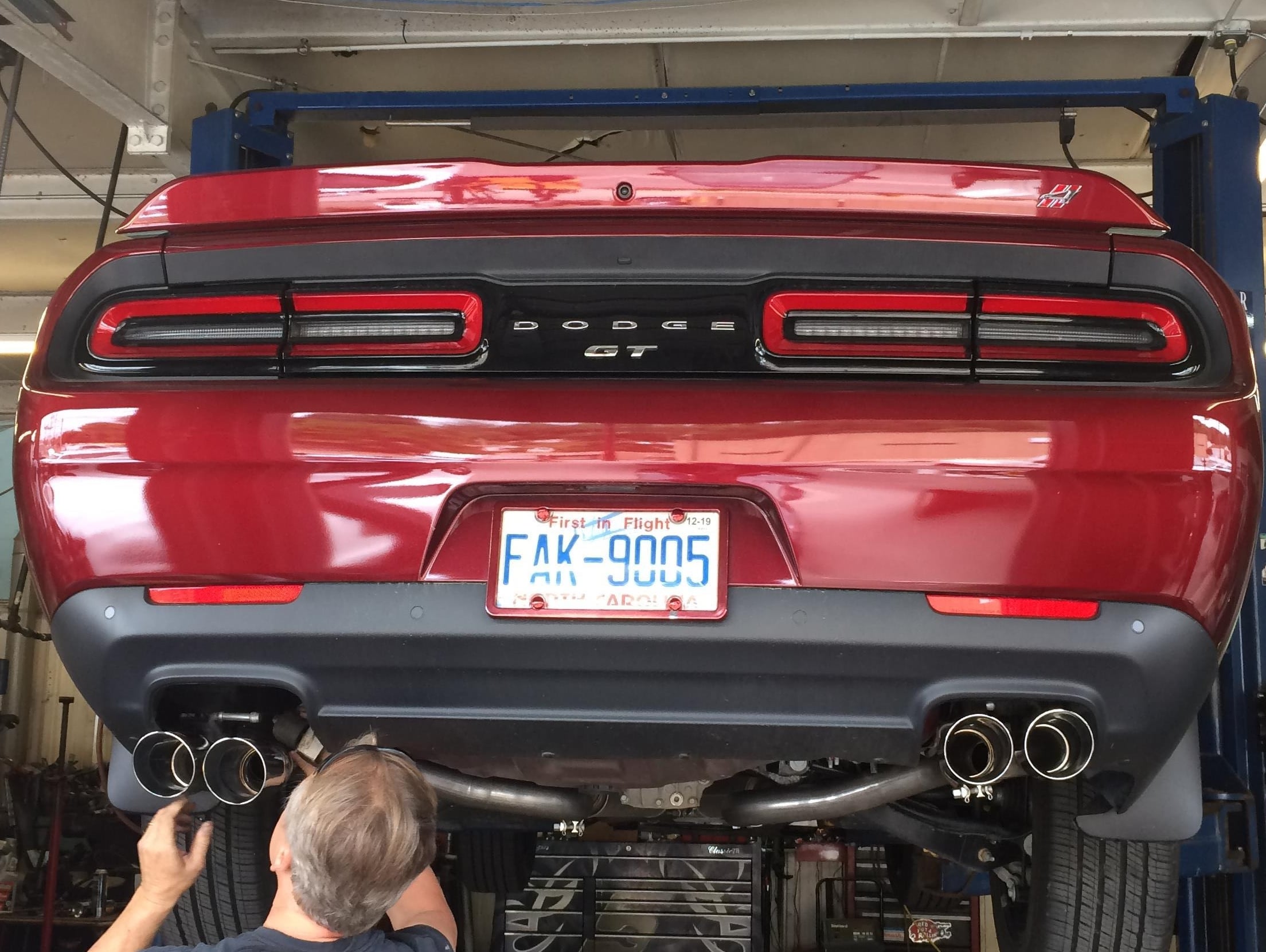 Technician installing a quad-tip cat-back exhaust system on a Dodge Challenger raised on a vehicle lift, showing stainless steel exhaust piping and performance mufflers.